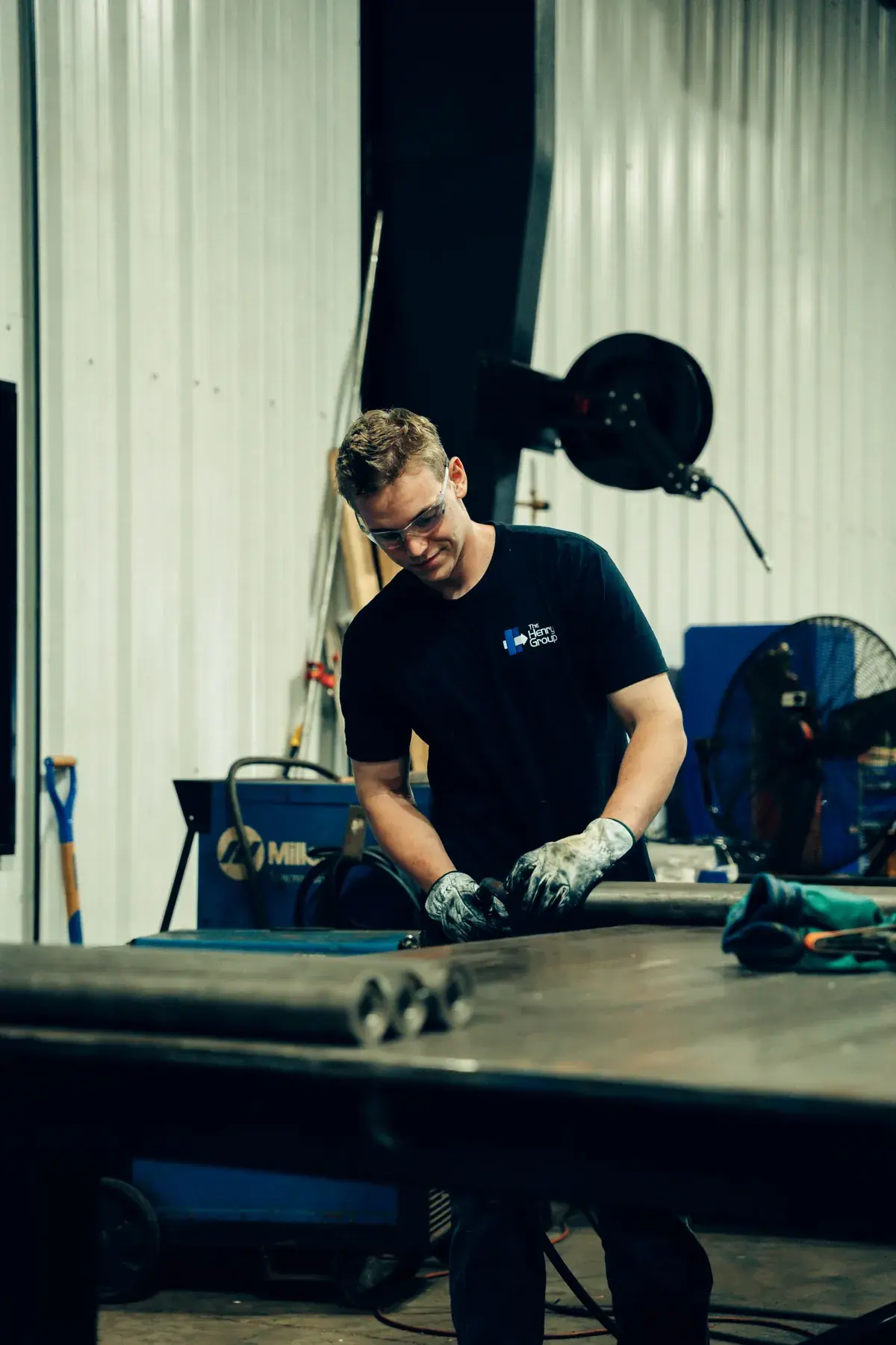 Fabricator wearing gloves handling a round tube component at the workbench.