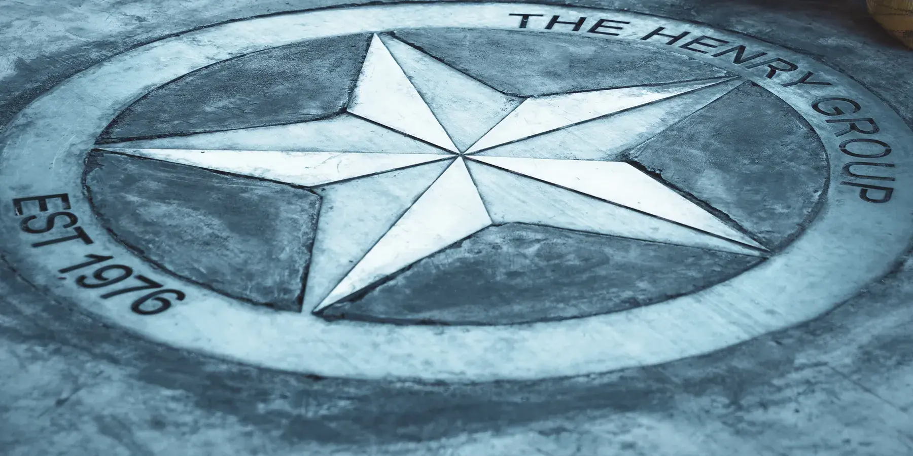 Metal emblem with a star, The Henry Group name and the date Est. 1976, resting on a workbench.