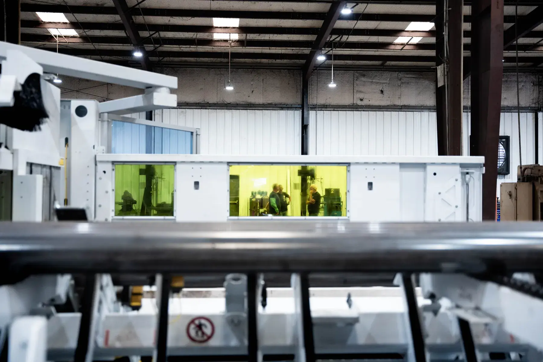 Tube laser enclosure with yellow protective windows and material handling rails in the foreground.