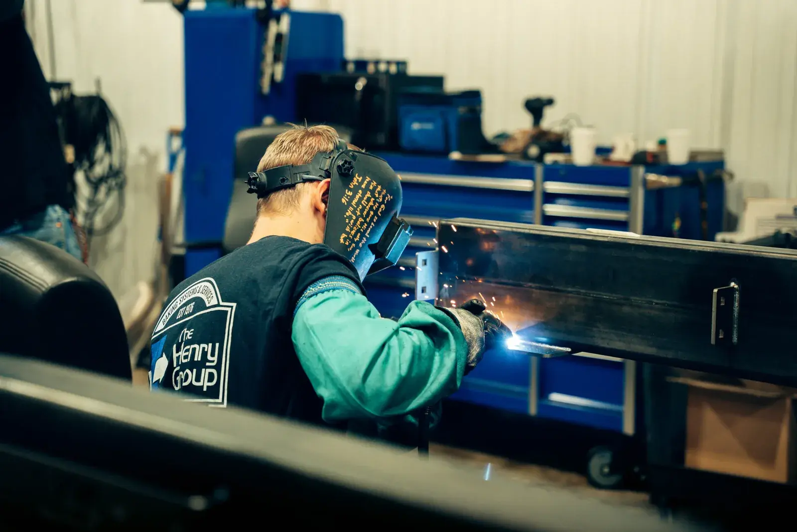 Welder in a helmet and gloves joining a metal assembly at the workbench.